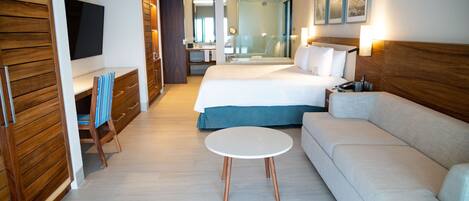 Una habitación de hotel con cama, sofá, televisor, escritorio y espejo.