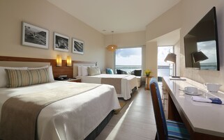 Una camera d'albergo con un letto grande, una scrivania, una sedia e vista sul mare.