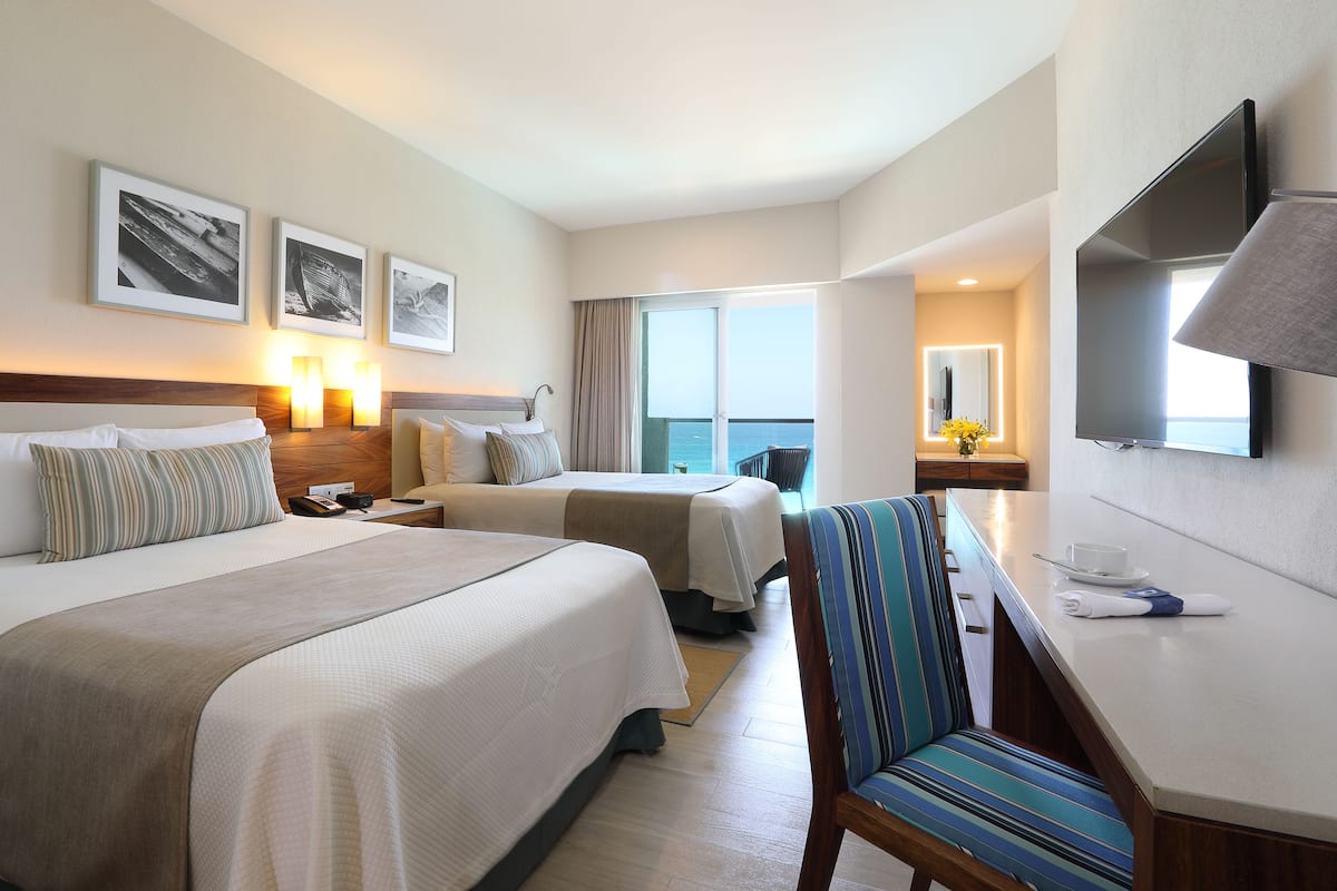 Habitación de hotel con dos camas, un escritorio, una silla, un televisor y un balcón con vistas.