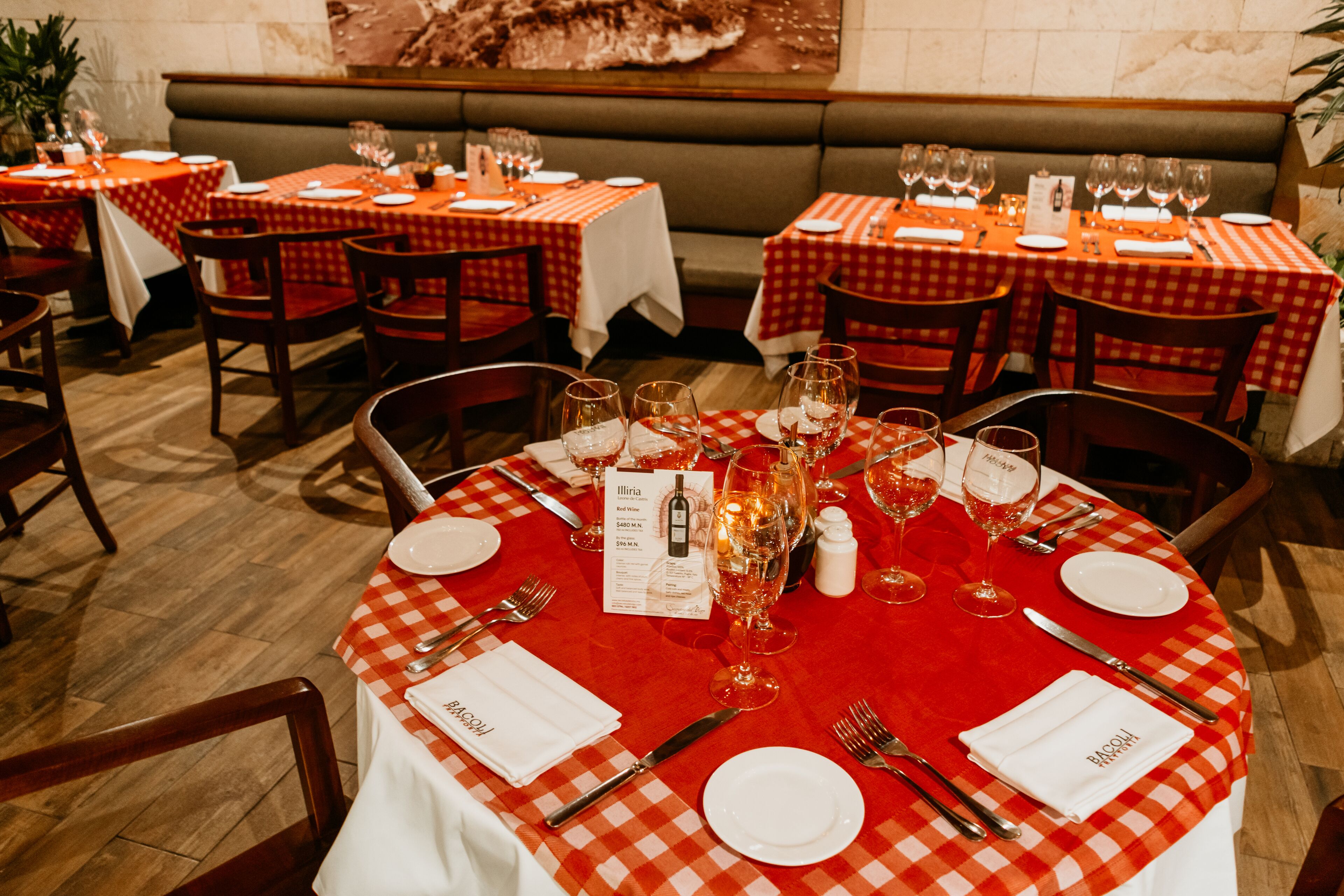 Un restaurante con manteles a cuadros rojos y blancos, mesas dispuestas con cuidado, copas de vino, platos y cubiertos.