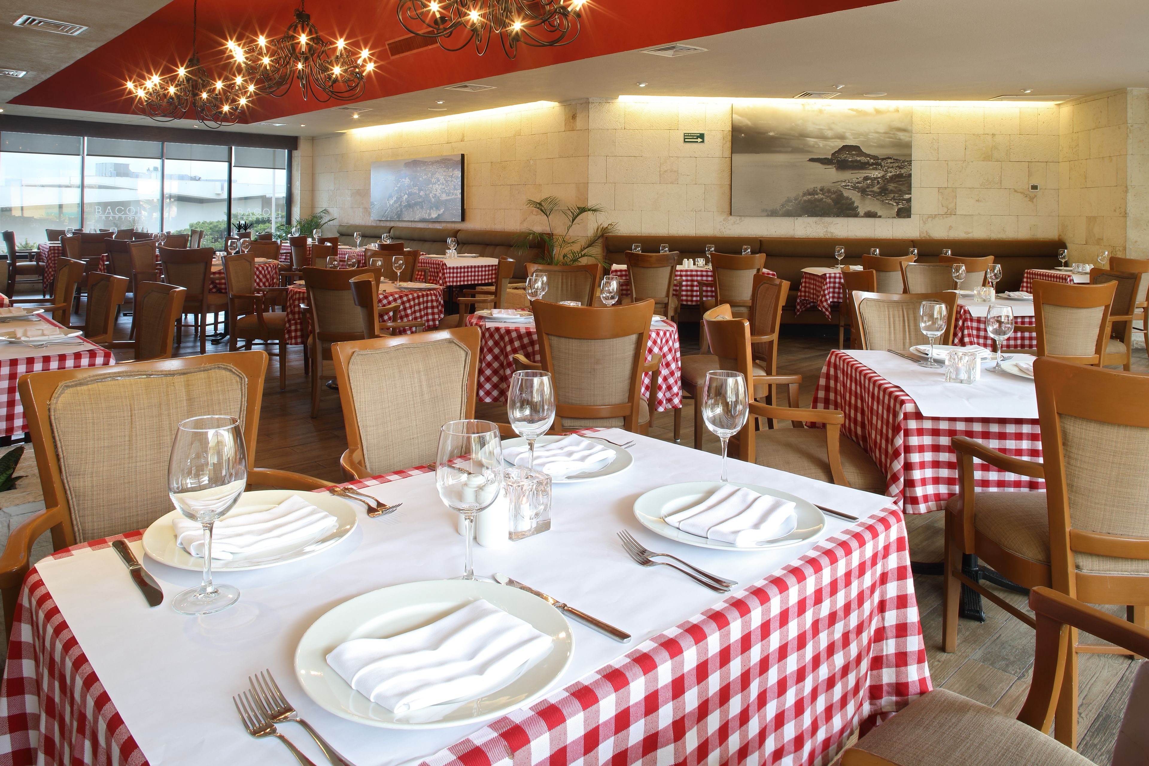 A restaurant with red and white checkered tablecloths, neatly set dining tables with plates, glasses, and cutlery.
