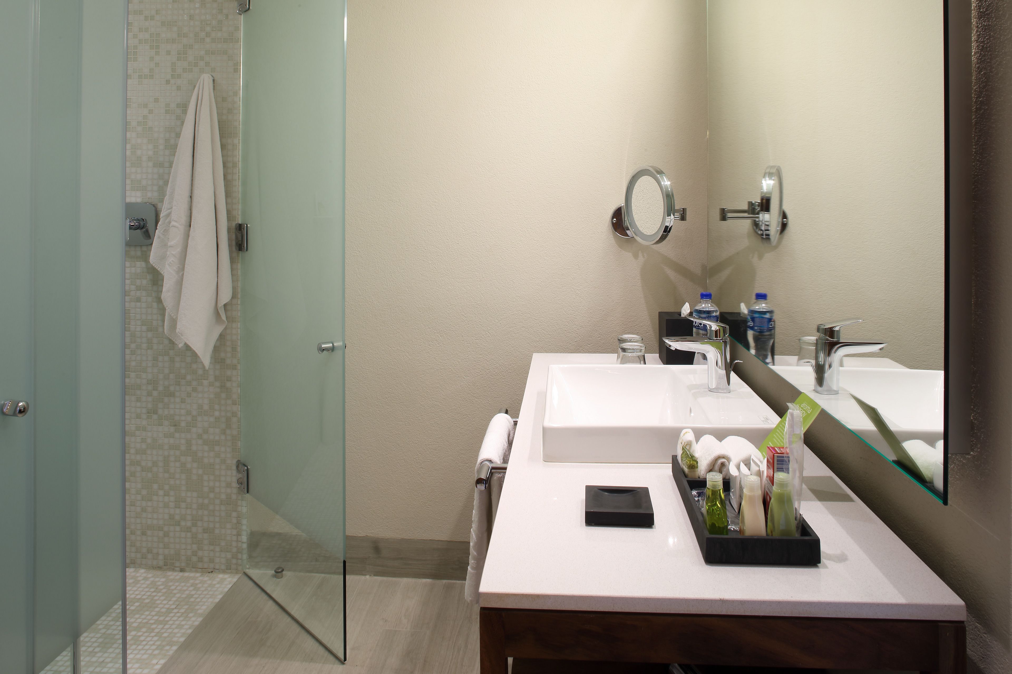 Baño con dos lavamanos, cabina de ducha con paredes de vidrio y un espejo.
