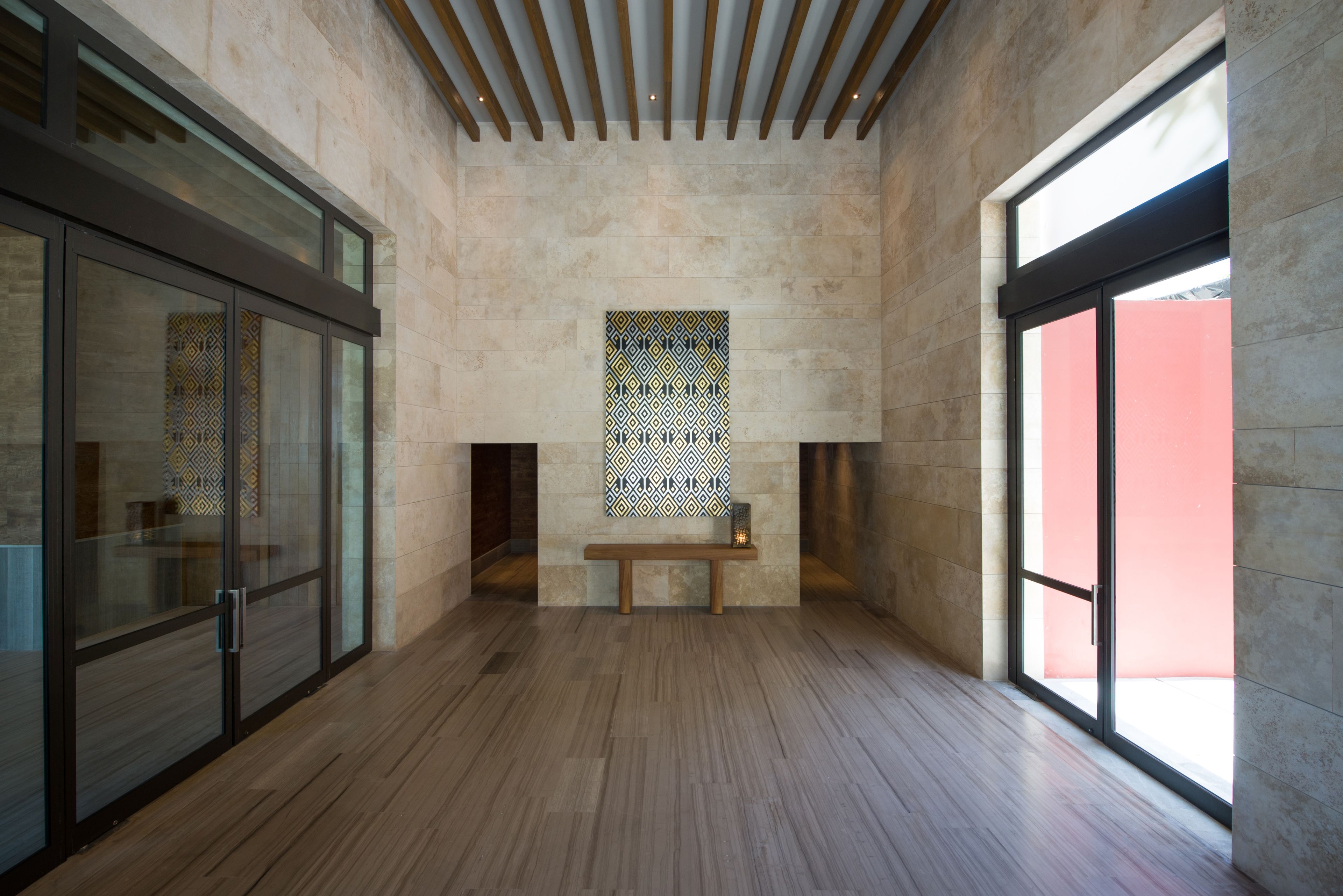 A spacious hallway with a wooden bench, a patterned wall, and large windows.