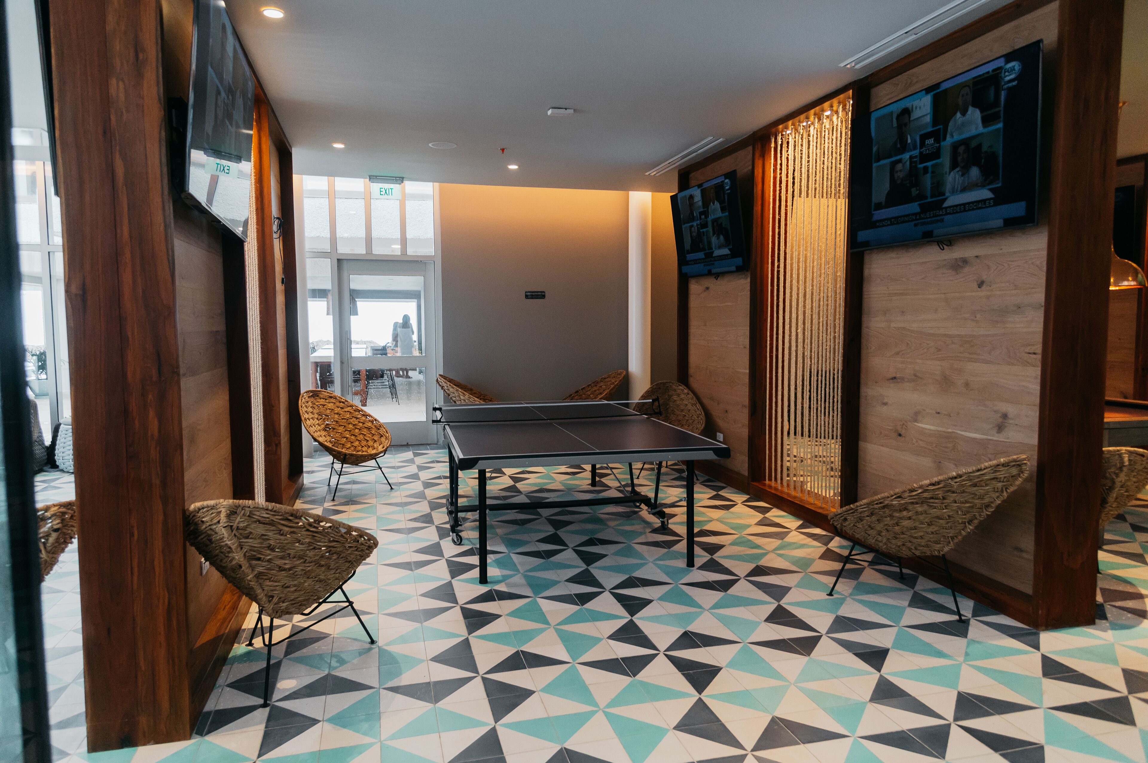 A room with a ping pong table, wicker chairs, and a patterned floor.