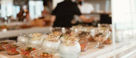 A buffet table with various dishes, including clear bowls with food and a glass jar with a blue substance.
