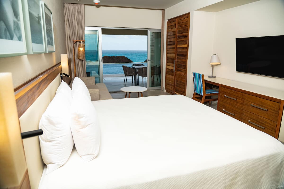Habitación de hotel con una cama grande, televisión, una mesita y vista al océano.