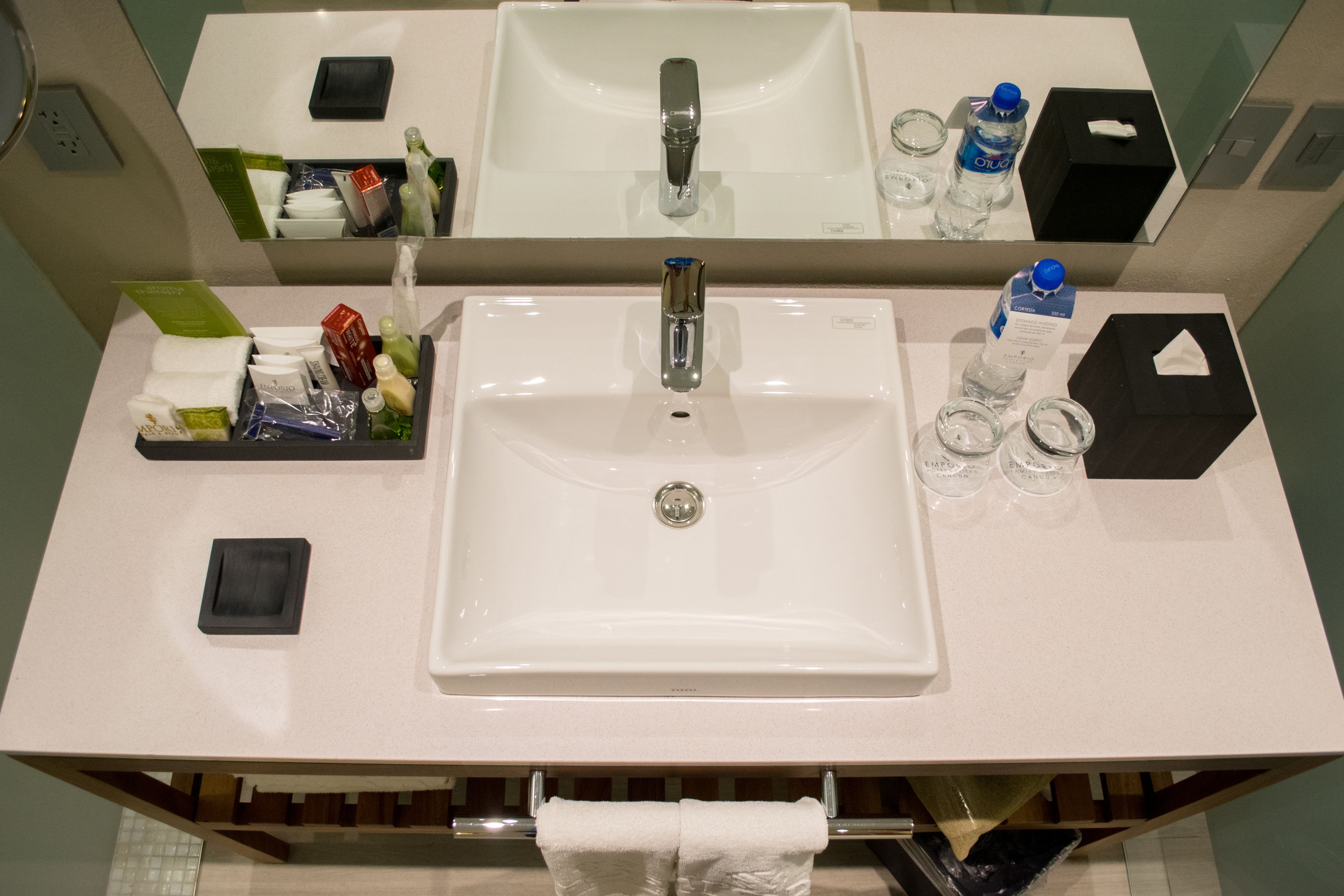Une salle de bain d’hôtel avec un lavabo blanc, un miroir et des articles de toilette.