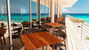 A seaside restaurant with wooden tables and chairs, large windows offering ocean views, and a balcony with a railing. - Emporio Cancun Optional All Inclusive (Cancun)