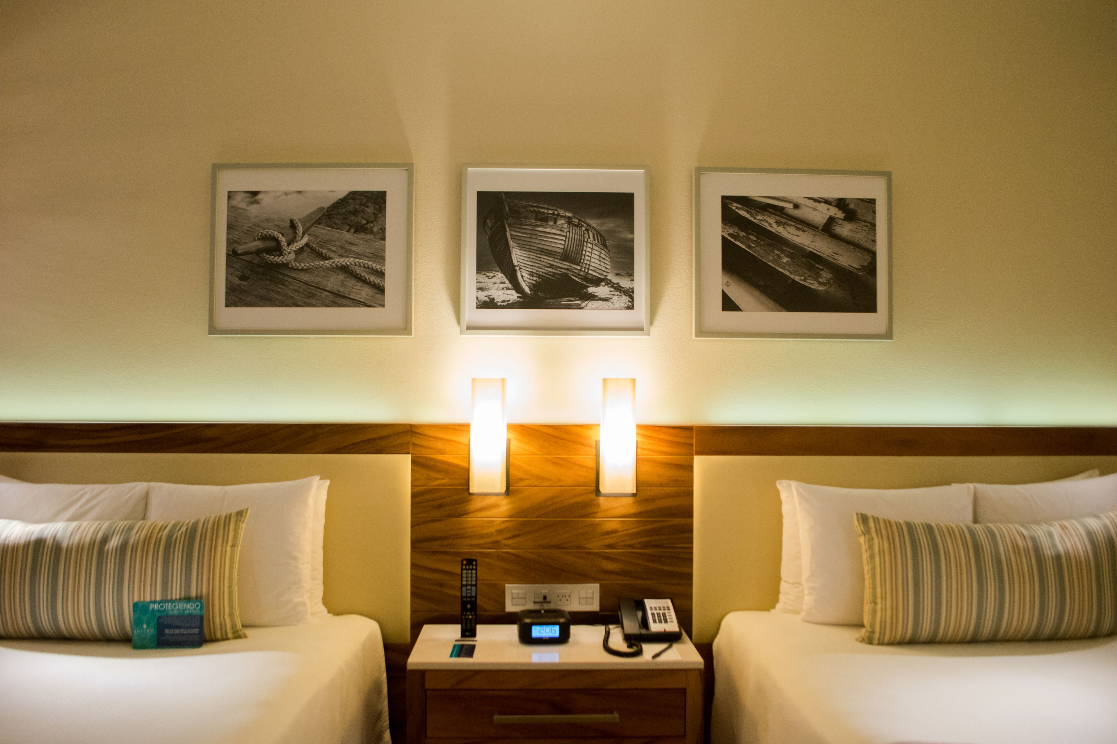 Ein Hotelzimmer mit zwei Betten, einem Nachttisch mit Telefon und Fernbedienung sowie drei gerahmten Bildern an der Wand.