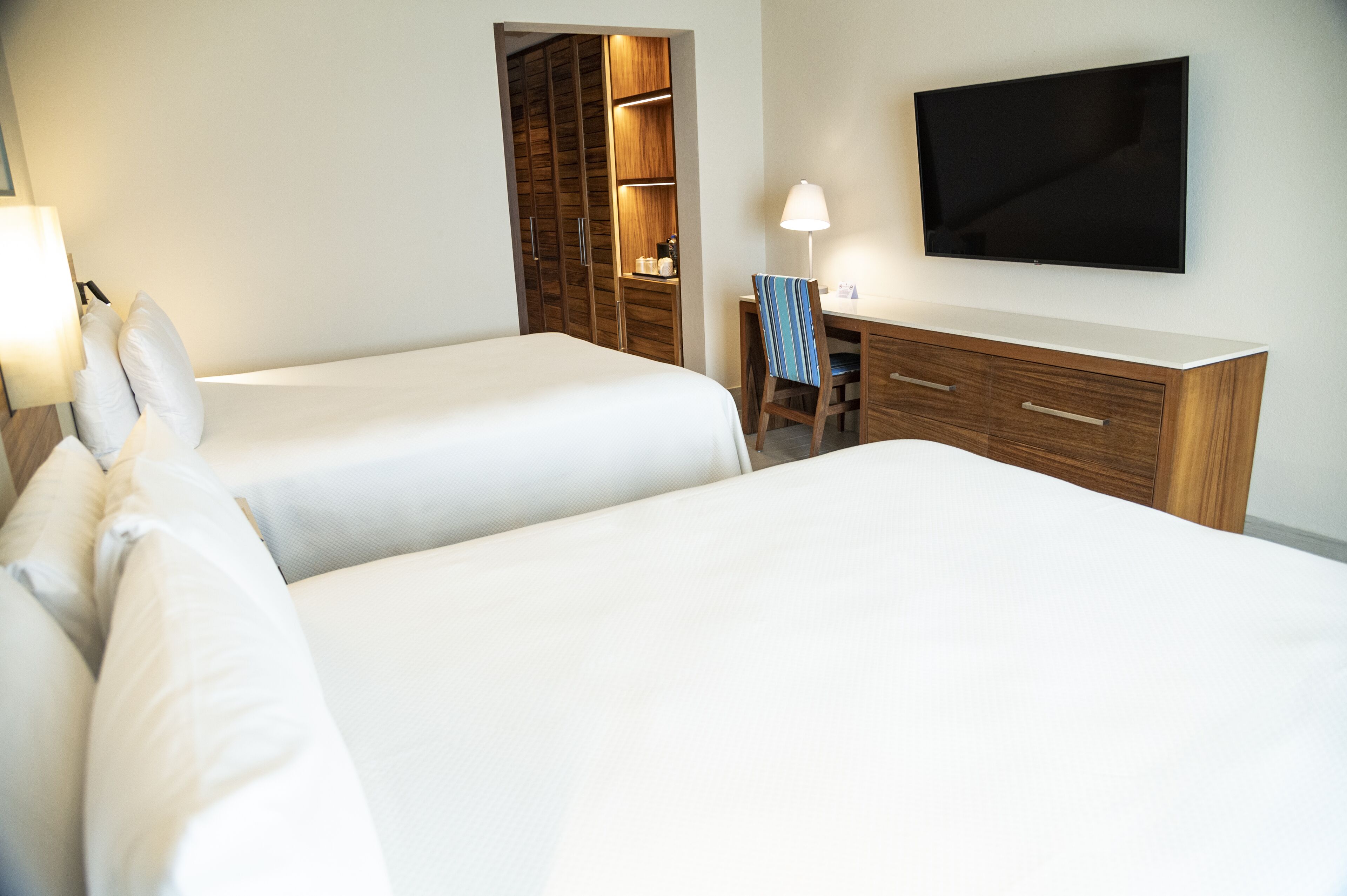 A hotel room with two beds, a desk, a chair, a TV, and a wardrobe.