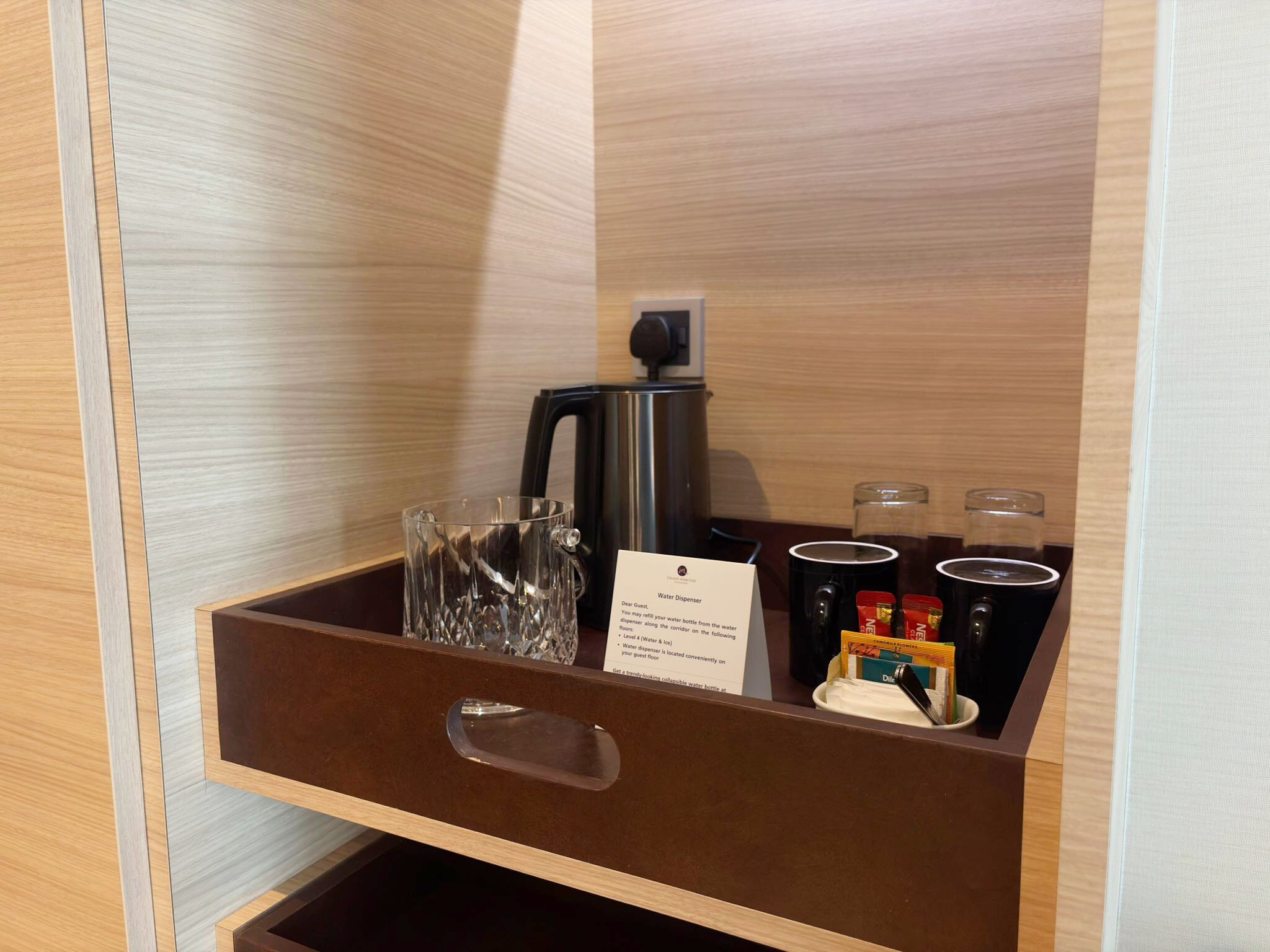 A water dispenser and coffee maker in a wooden cabinet with a drawer below.