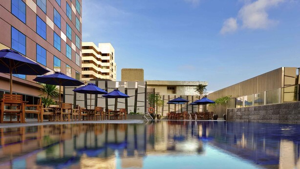 A hotel pool with lounge chairs and umbrellas, surrounded by buildings. - Grand Mercure Singapore Roxy (Singapore)