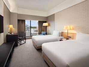 A hotel room with two beds, a desk, a chair, a TV, and a window with a view of buildings. - Grand Mercure Singapore Roxy (Singapore)