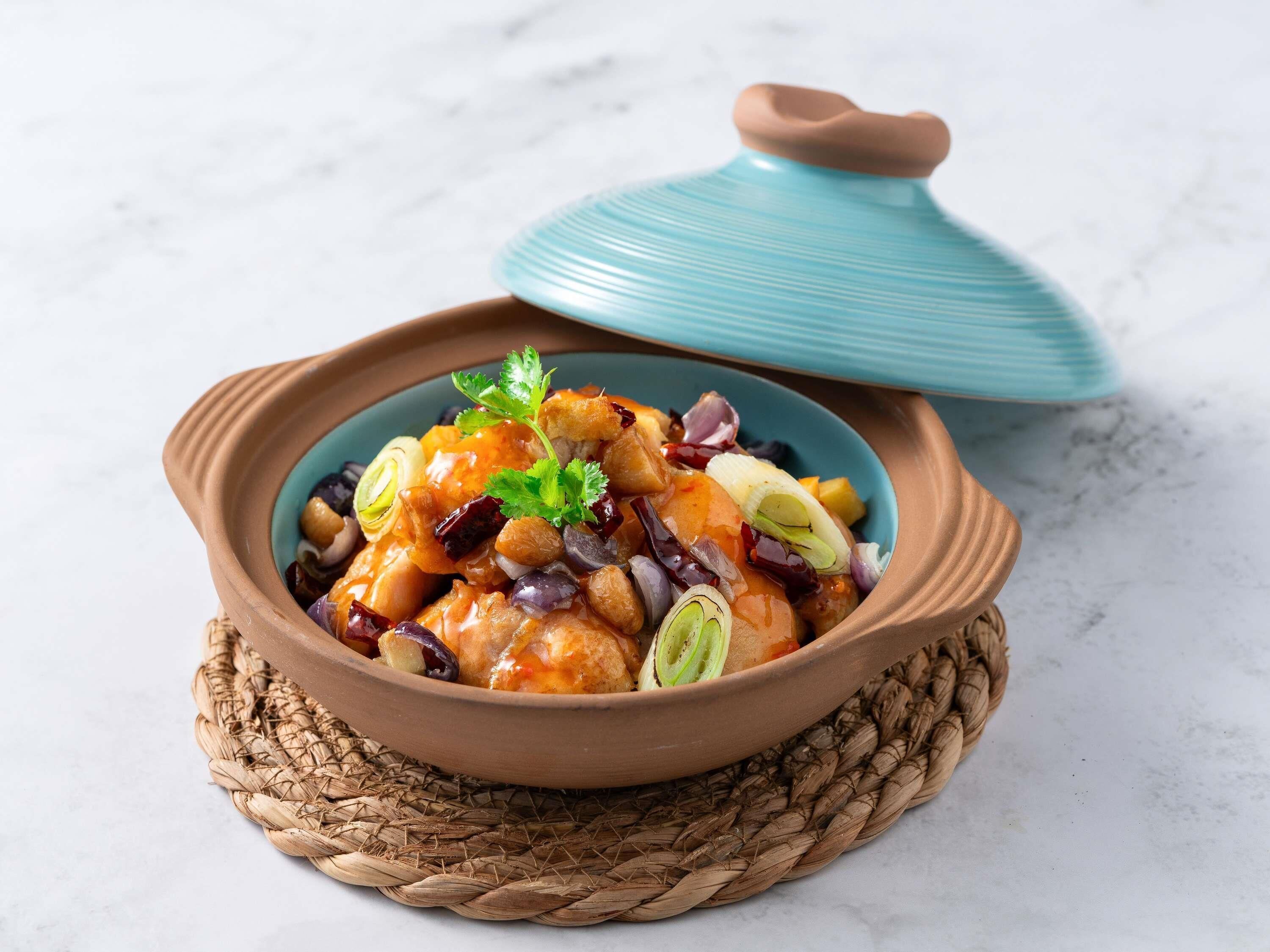 Un piatto in terracotta con coperchio, adagiato su un sottile tappetino intrecciato.