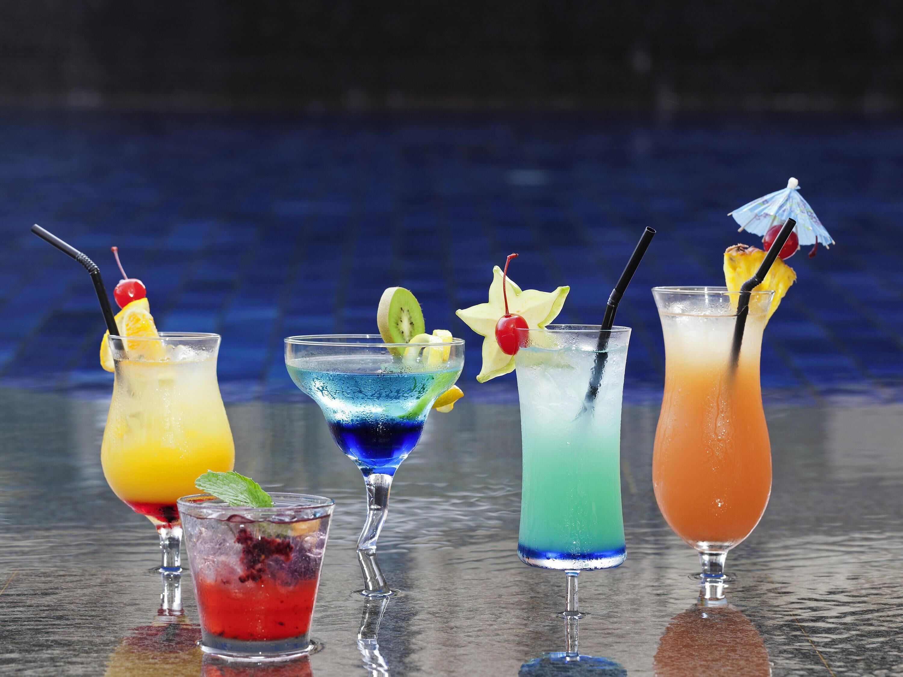 Five cocktails with various garnishes on a reflective surface.
