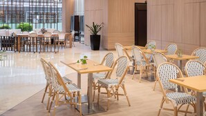 A modern dining area with wooden tables and wicker chairs, large windows, and a potted plant. - Grand Mercure Singapore Roxy (Singapore)