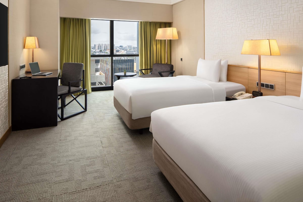 Habitación de hotel con dos camas, un escritorio con una computadora portátil, una silla, una mesita y vista a la ciudad.