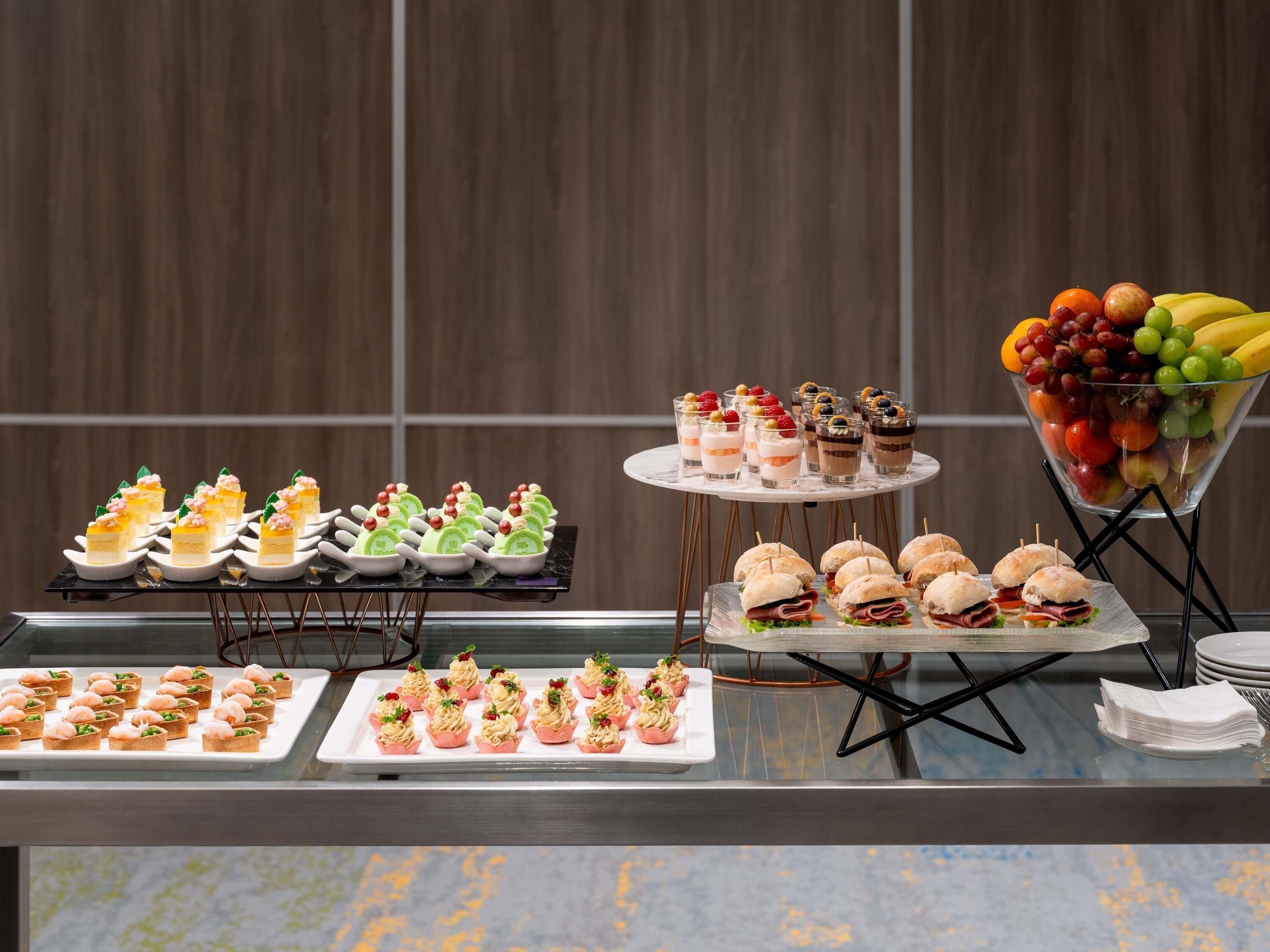 A buffet with various food items, including sandwiches, desserts, and fruit.