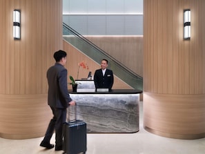 A hotel reception desk with a nameplate, a potted plant, and a person walking with a suitcase. - Grand Mercure Singapore Roxy (Singapore)