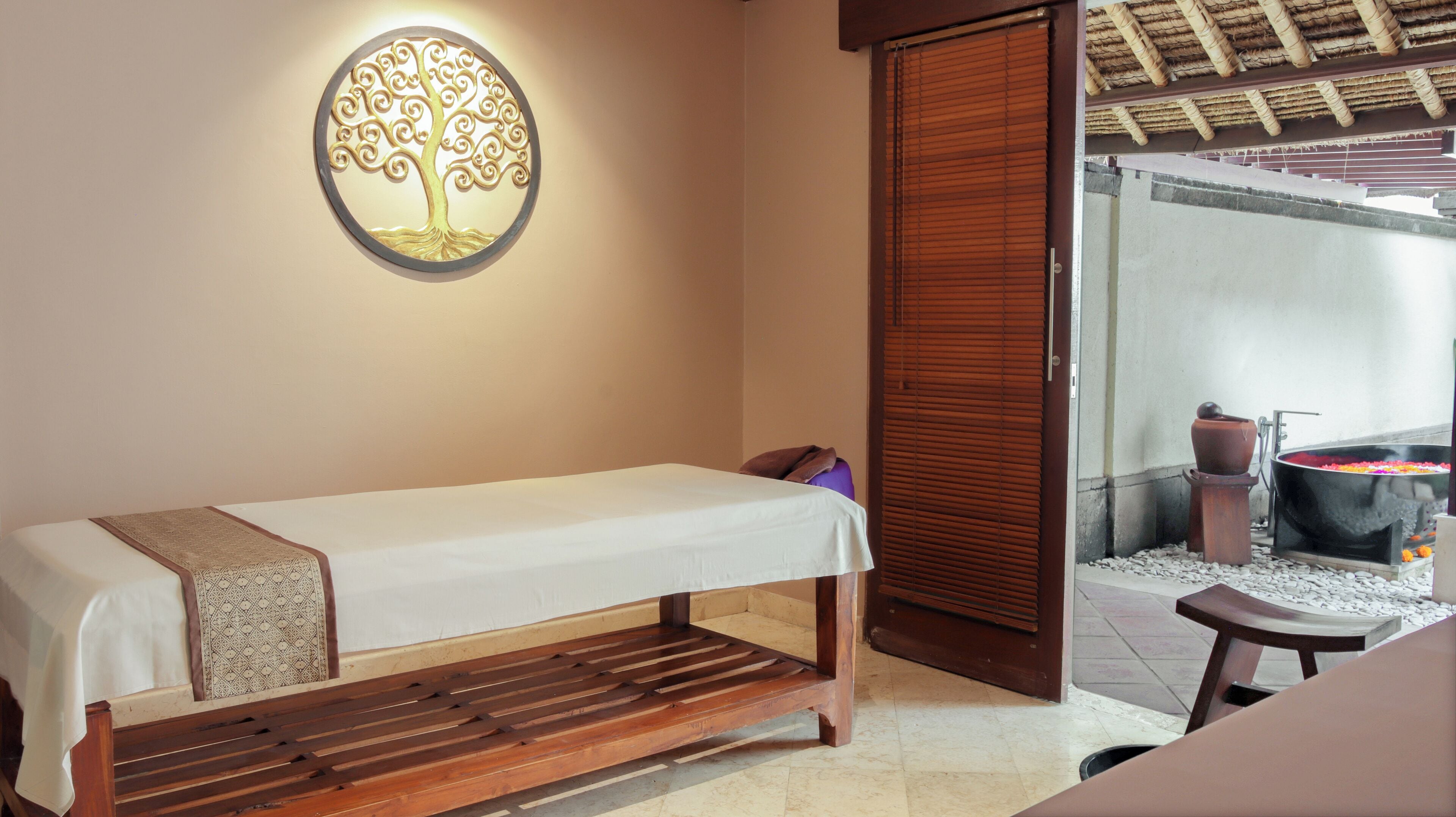A room with a wooden bench, a wall-mounted light fixture, and a view of a spa area with a hot tub.