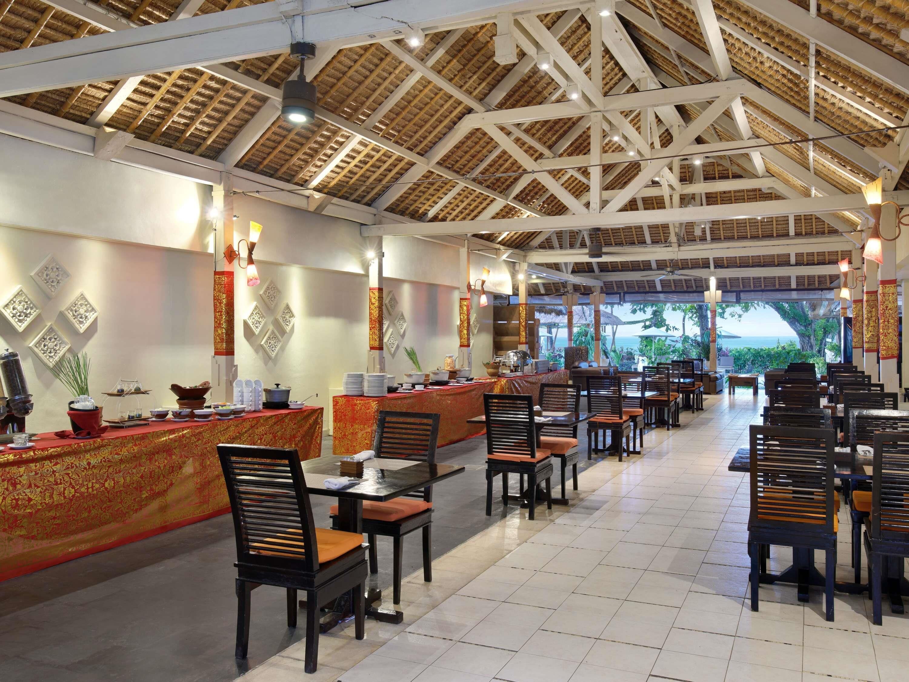 Een restaurant met een hoge plafond en houten balken, met een buffetopstelling met diverse gerechten en een balie. Tafels en stoelen staan klaar voor diners.