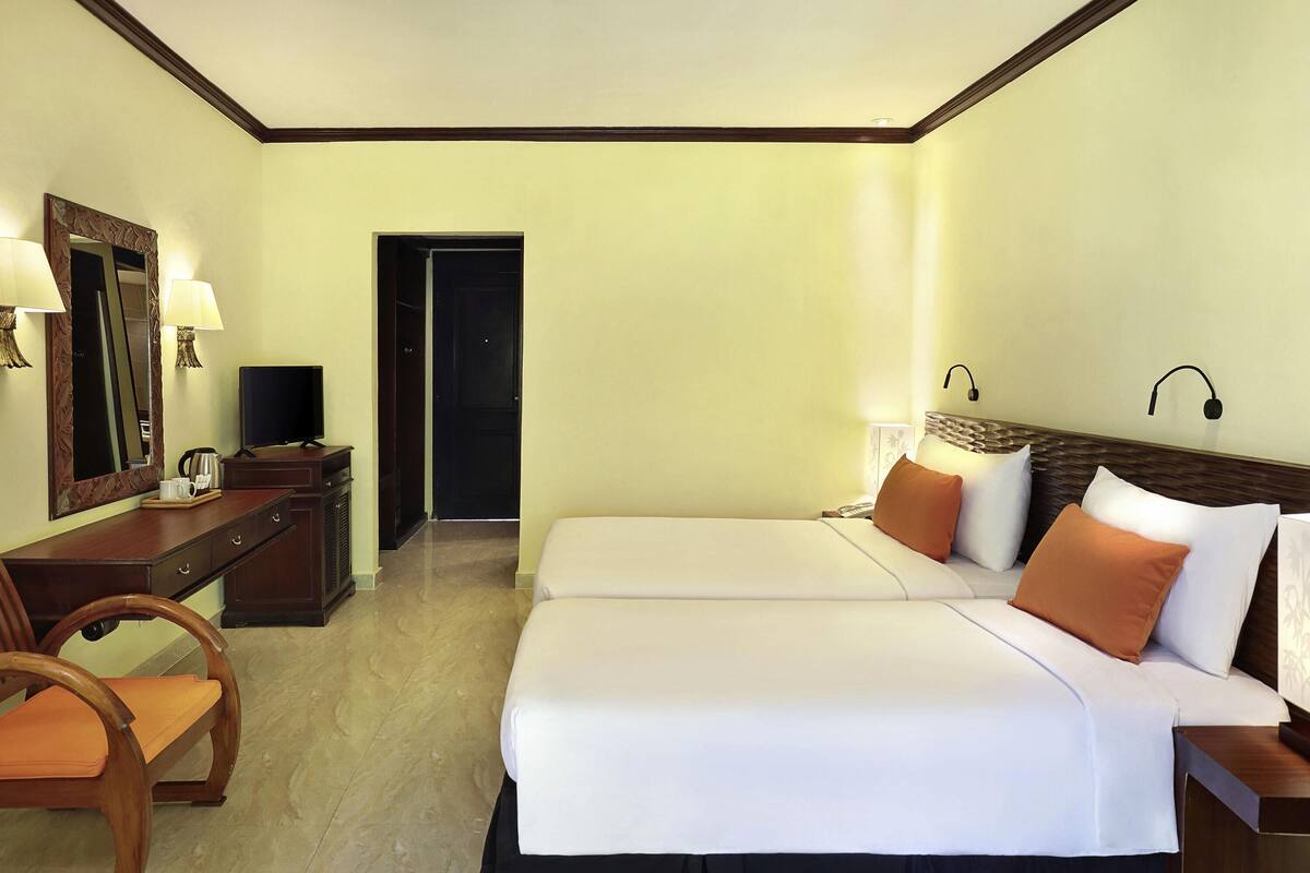 A hotel room with two beds, a desk, a chair, a television, and a mirror.