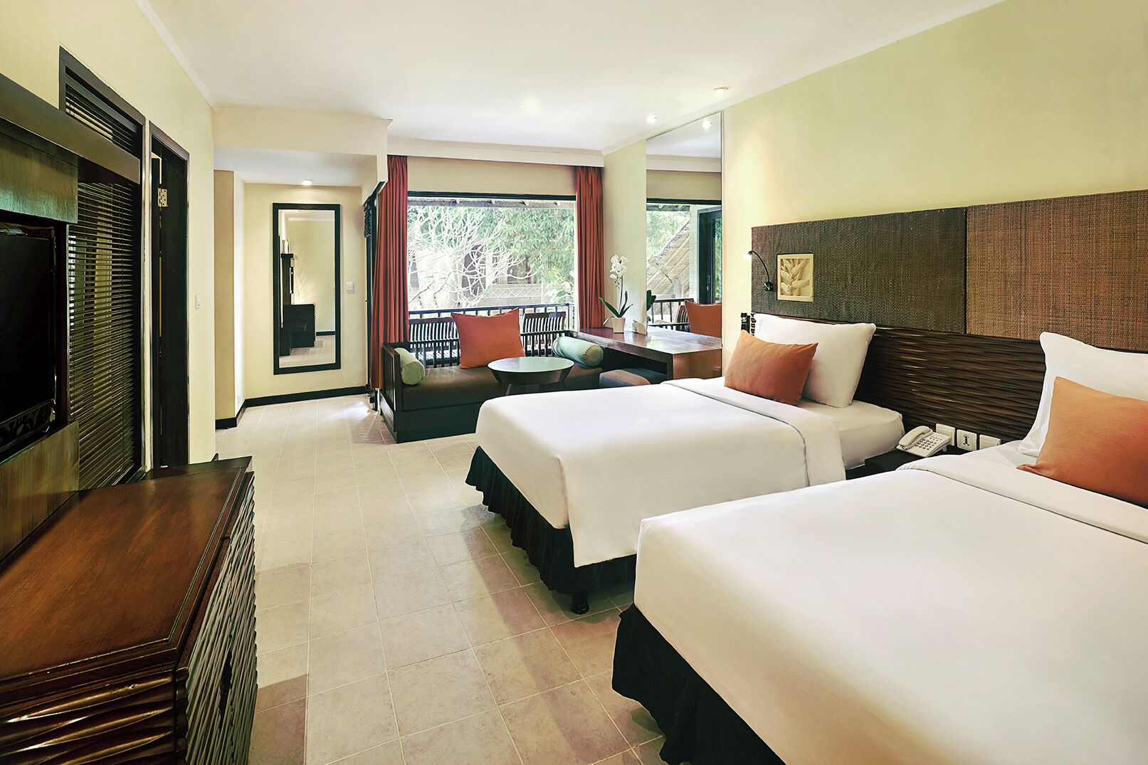 Habitación de hotel con dos camas, televisor, escritorio y balcón con vista a árboles.