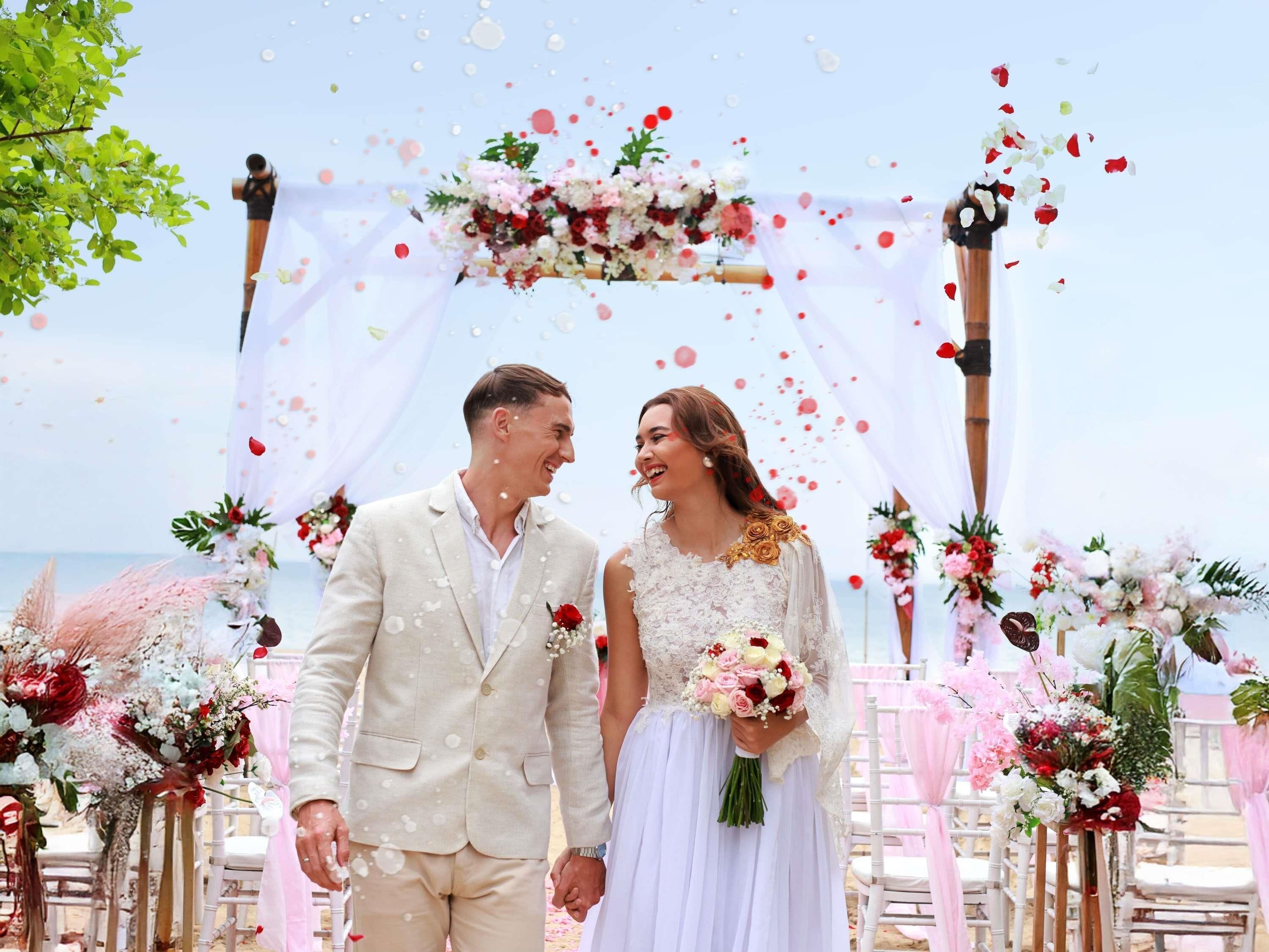 Une cérémonie de mariage avec une arche fleurie et des invités assis sur des chaises blanches.
