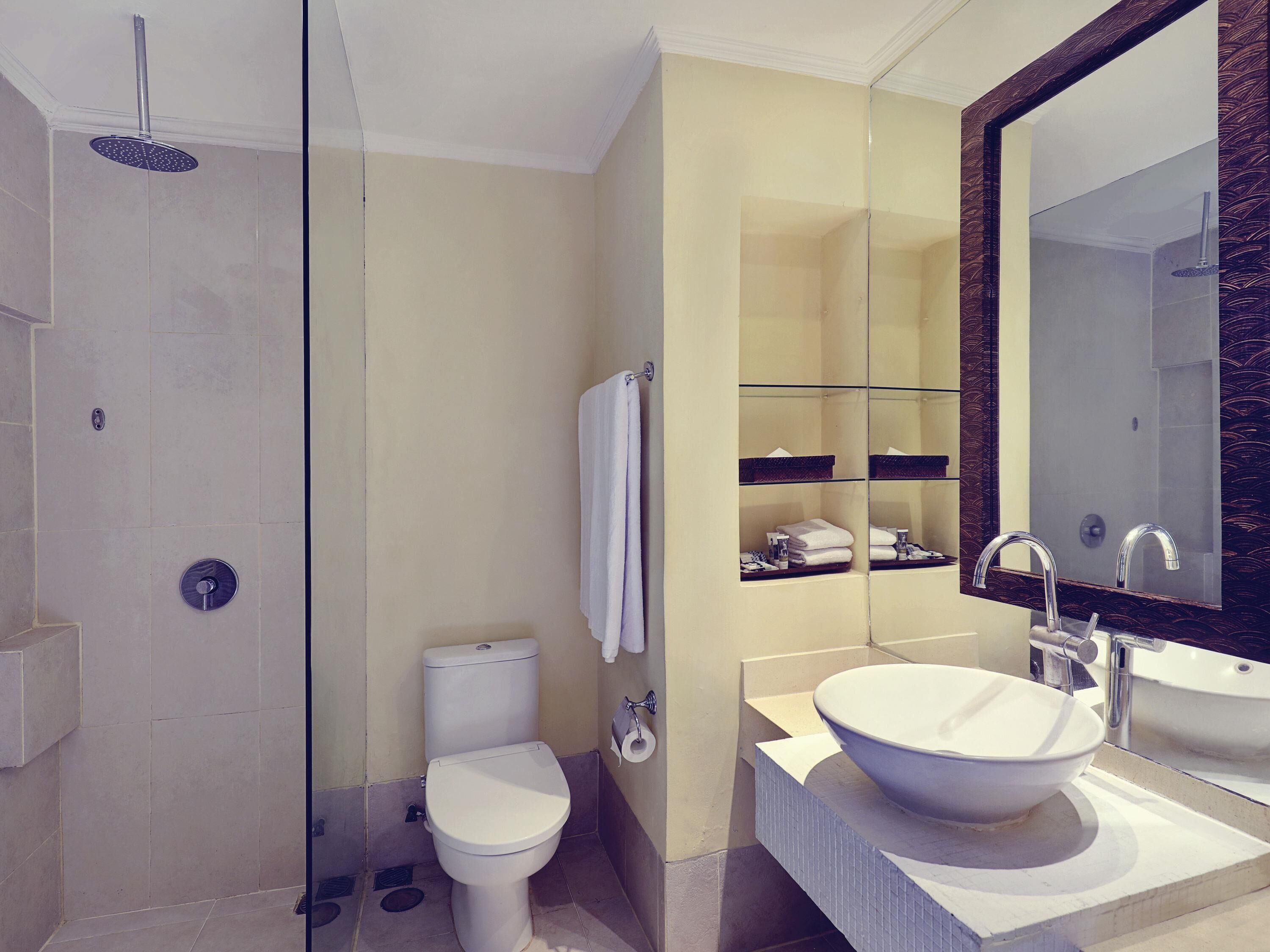 A modern bathroom with a glass-enclosed shower, a toilet, a sink with a large basin, and a mirror with a decorative frame.