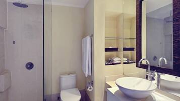 A modern bathroom with a glass-enclosed shower, a toilet, a sink with a large basin, and a mirror with a decorative frame.