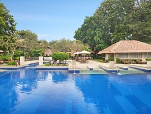 A swimming pool with lounge chairs and umbrellas, surrounded by trees and buildings. - Mercure Resort Sanur (Denpasar)