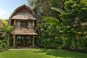 Un bâtiment à deux étages, doté d’un toit de chaume, d’un balcon et d’un jardin planté de végétaux tropicaux.
