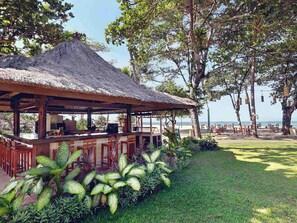 A beachside bar with a thatched roof, surrounded by lush greenery and overlooking the sea. - Mercure Resort Sanur (Denpasar)