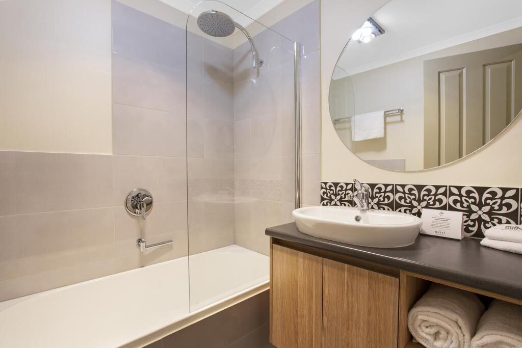 A modern bathroom with a glass-enclosed shower, a white bathtub, and a vanity with a sink and towel storage.