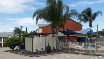 A fenced outdoor area with a pool, palm trees, and a building in the background.