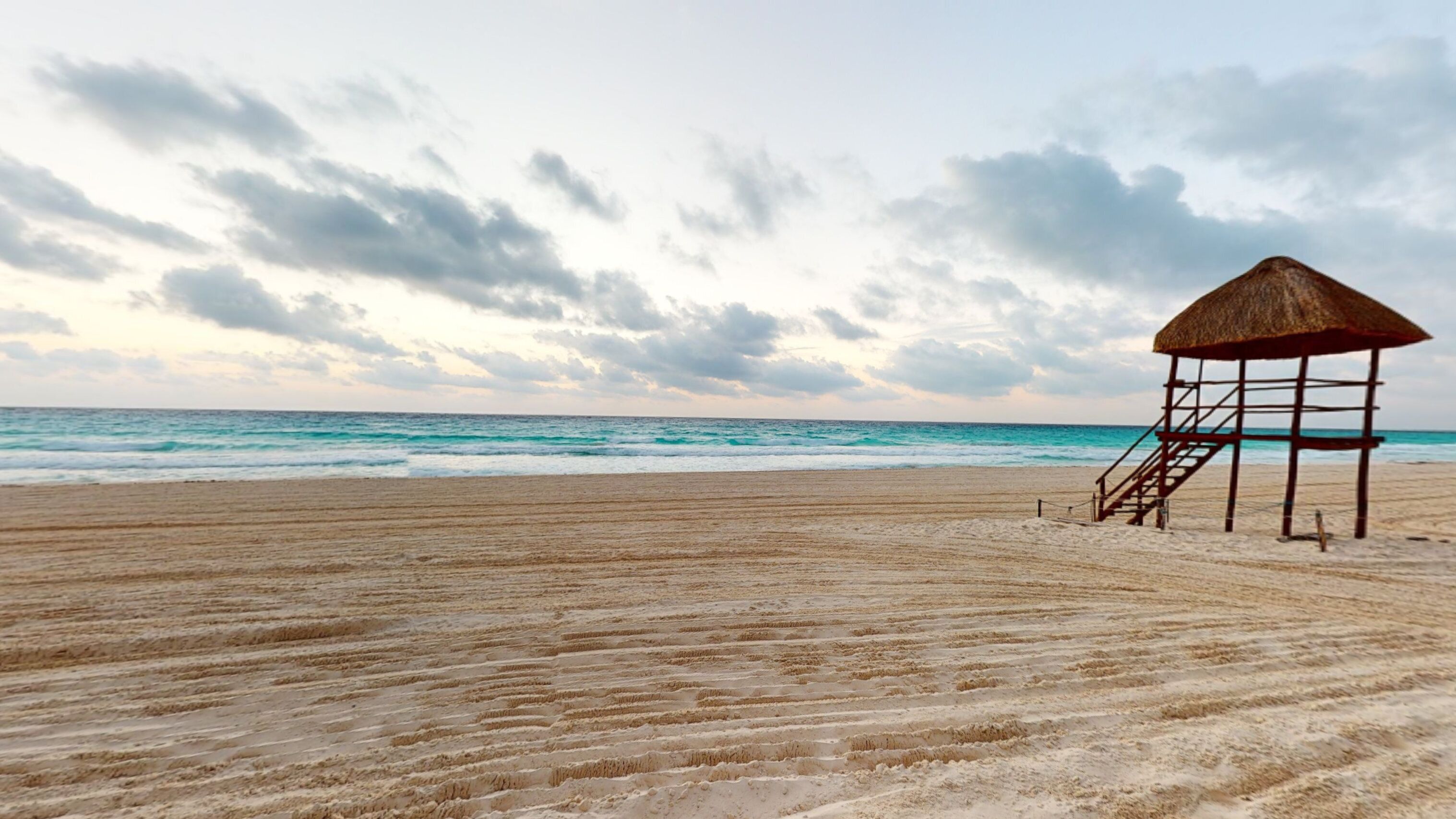 A beach with a wooden structure and a staircase leading to a thatched roof.