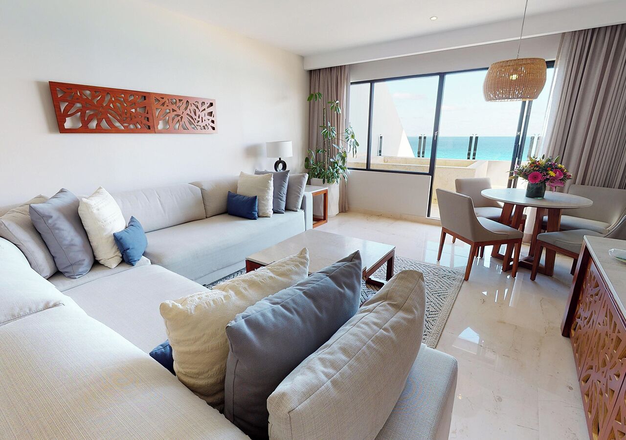 Un salon moderne comprenant un ensemble de canapés, un coin repas avec une table et des chaises, et une grande fenêtre donnant sur la mer.