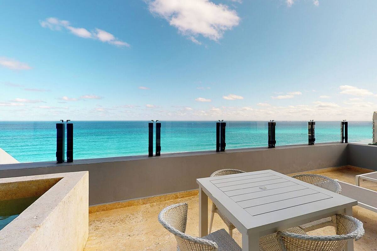 A terrace with a view of the ocean, featuring a table and chairs, and a concrete planter.