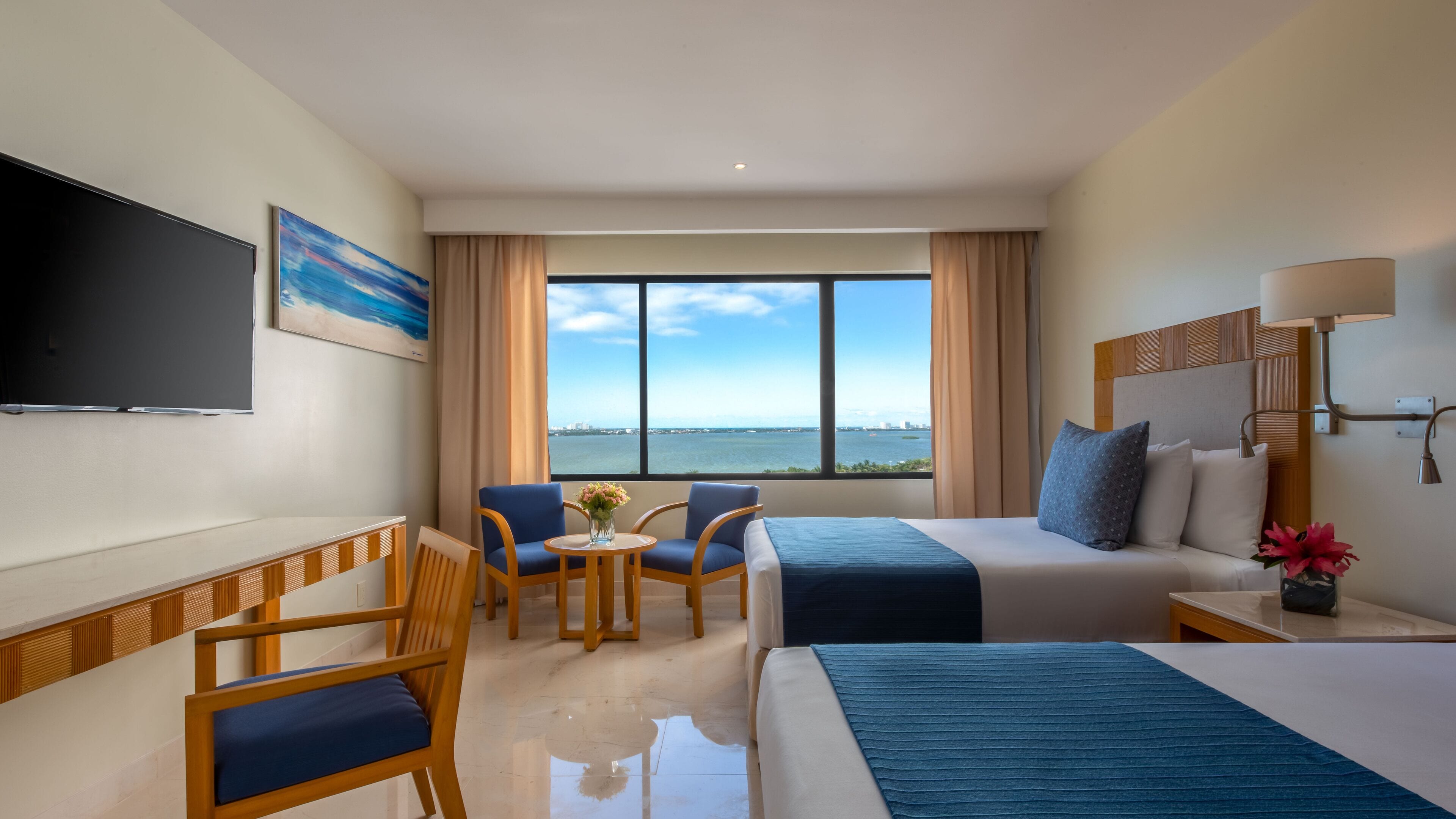A hotel room with a bed, a desk, a chair, a TV, and a view of the sea.