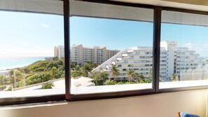 A view from a window overlooking a beachfront hotel with multiple buildings, palm trees, and a clear blue sky.