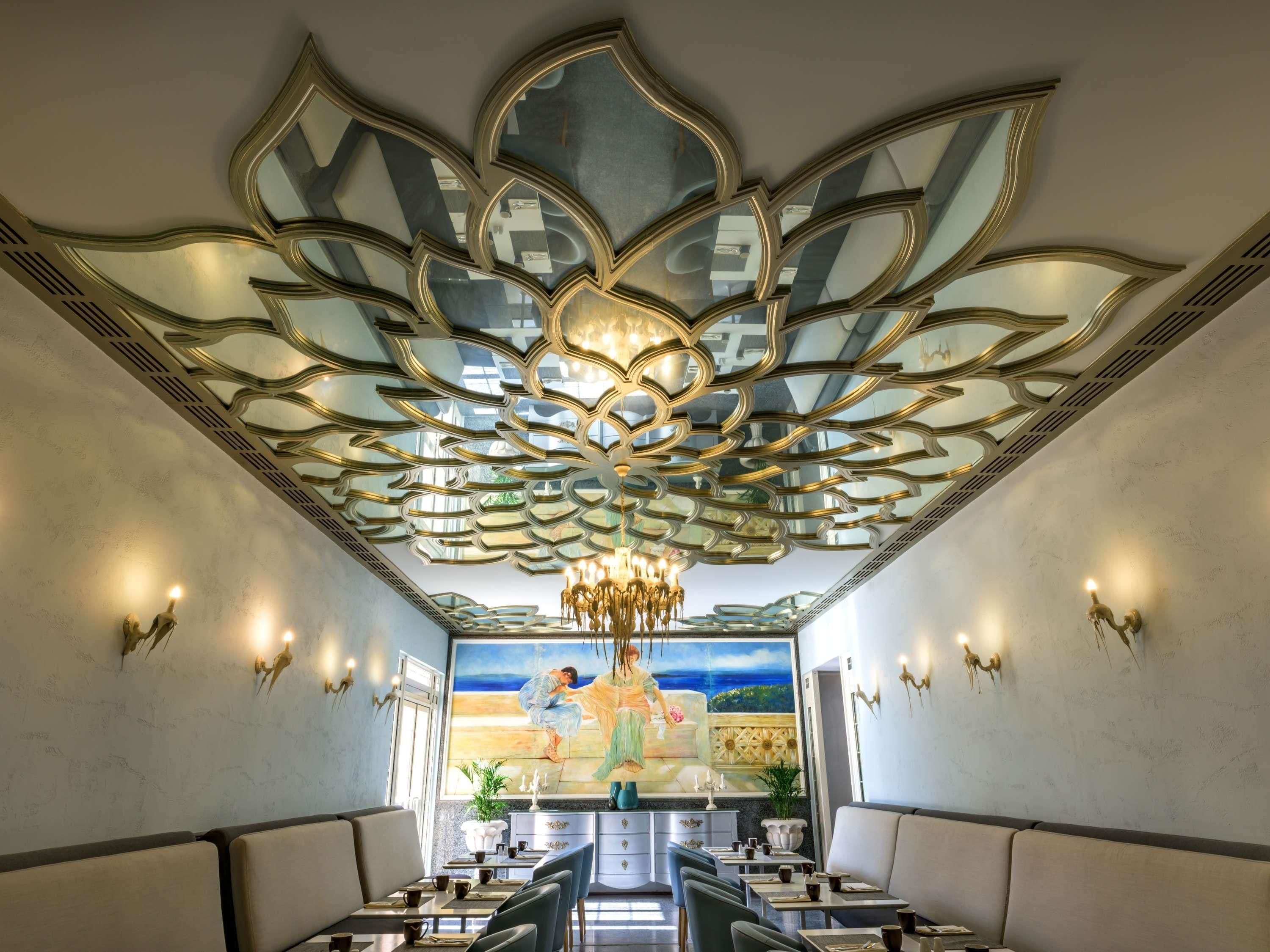 En restaurant med et lotus-dekoreret loft, et stort vægmaleri og en lysekrone.
