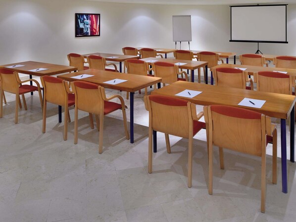 A classroom with wooden tables and chairs, a whiteboard, a projector screen, and a framed picture on the wall. - Mövenpick Resort & Residences Aqaba (Aqaba)