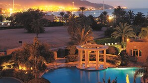 Un resort con piscina, palmeras y vista al mar al atardecer.