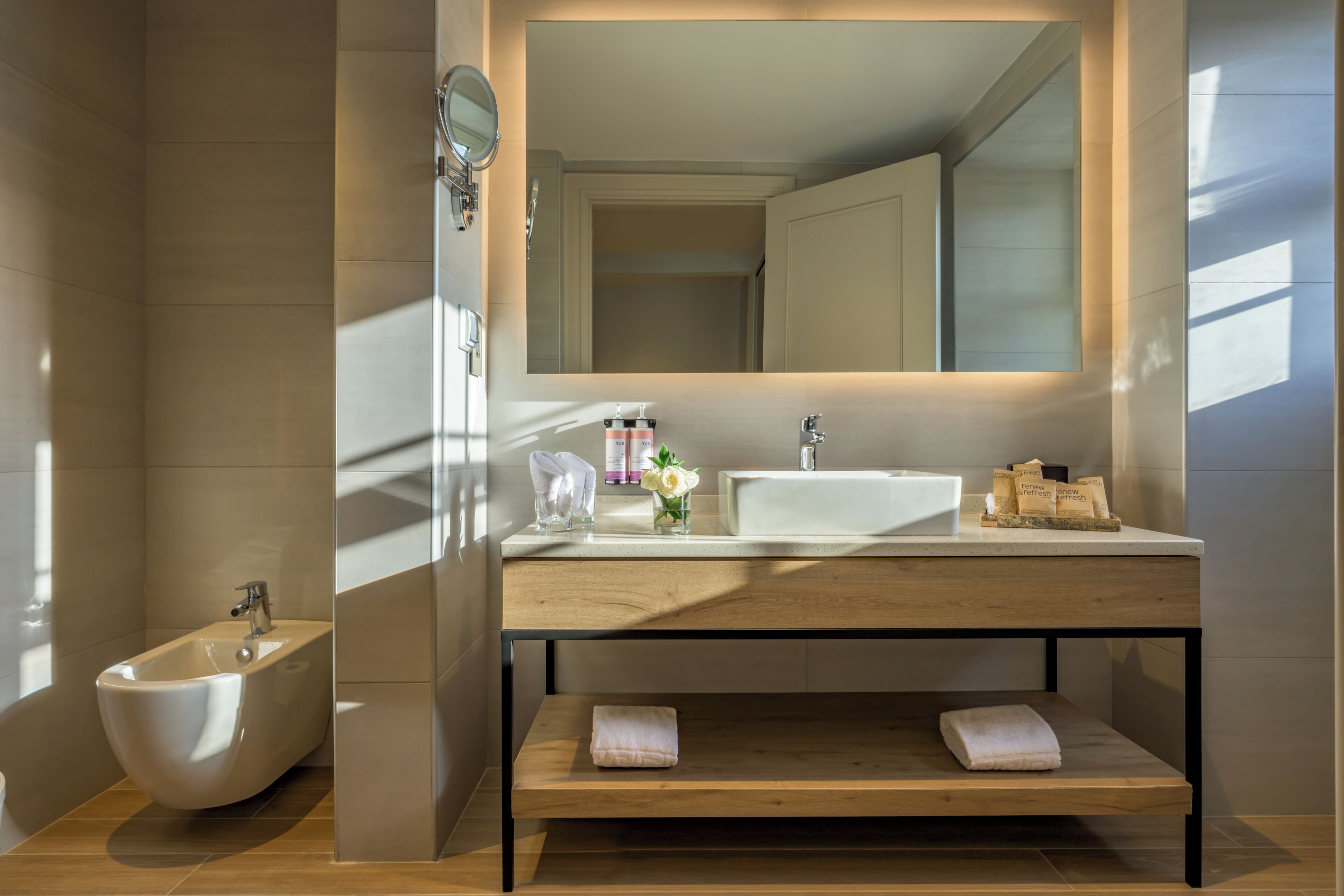 A modern bathroom with a bidet, a sink, a mirror, and a shelf with towels.