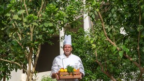 A chef carrying a tray of fresh produce in a garden setting with labeled plants. - Mövenpick Resort & Residences Aqaba (Aqaba)