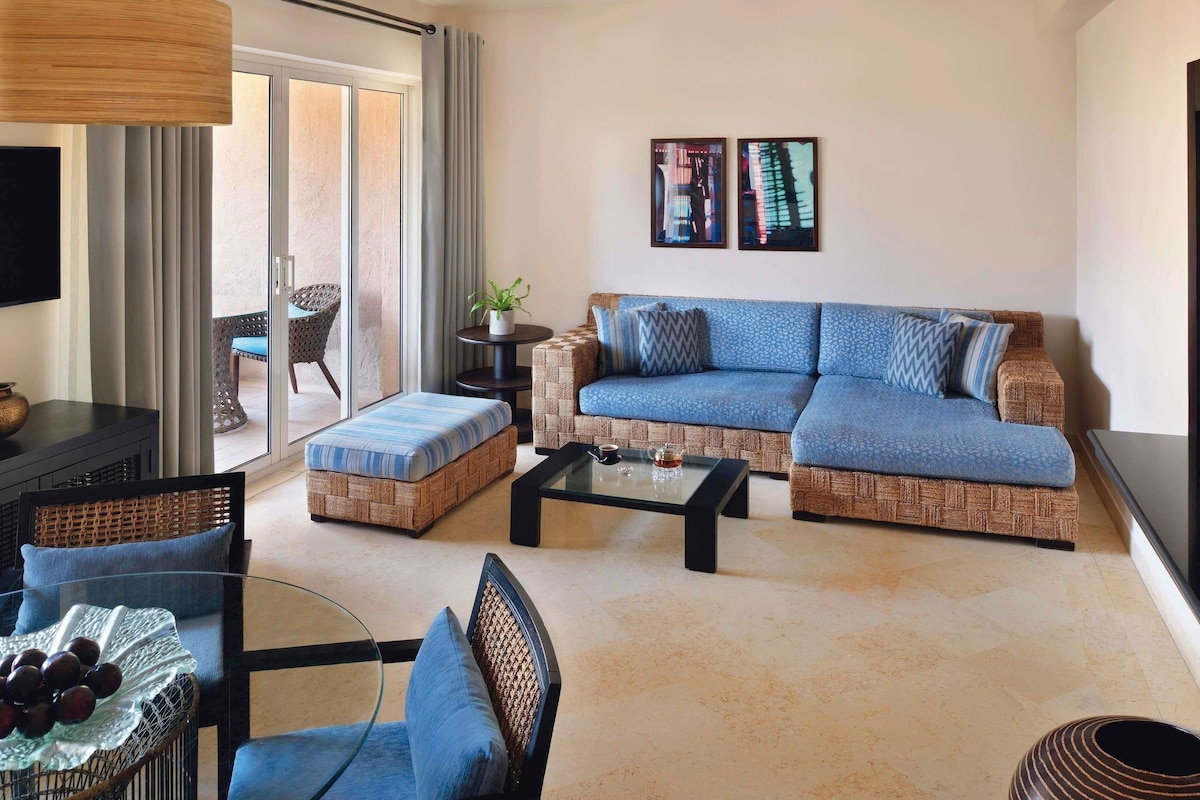 Un salon comprenant un canapé, un pouf, une table basse et un fauteuil avec une table en verre.