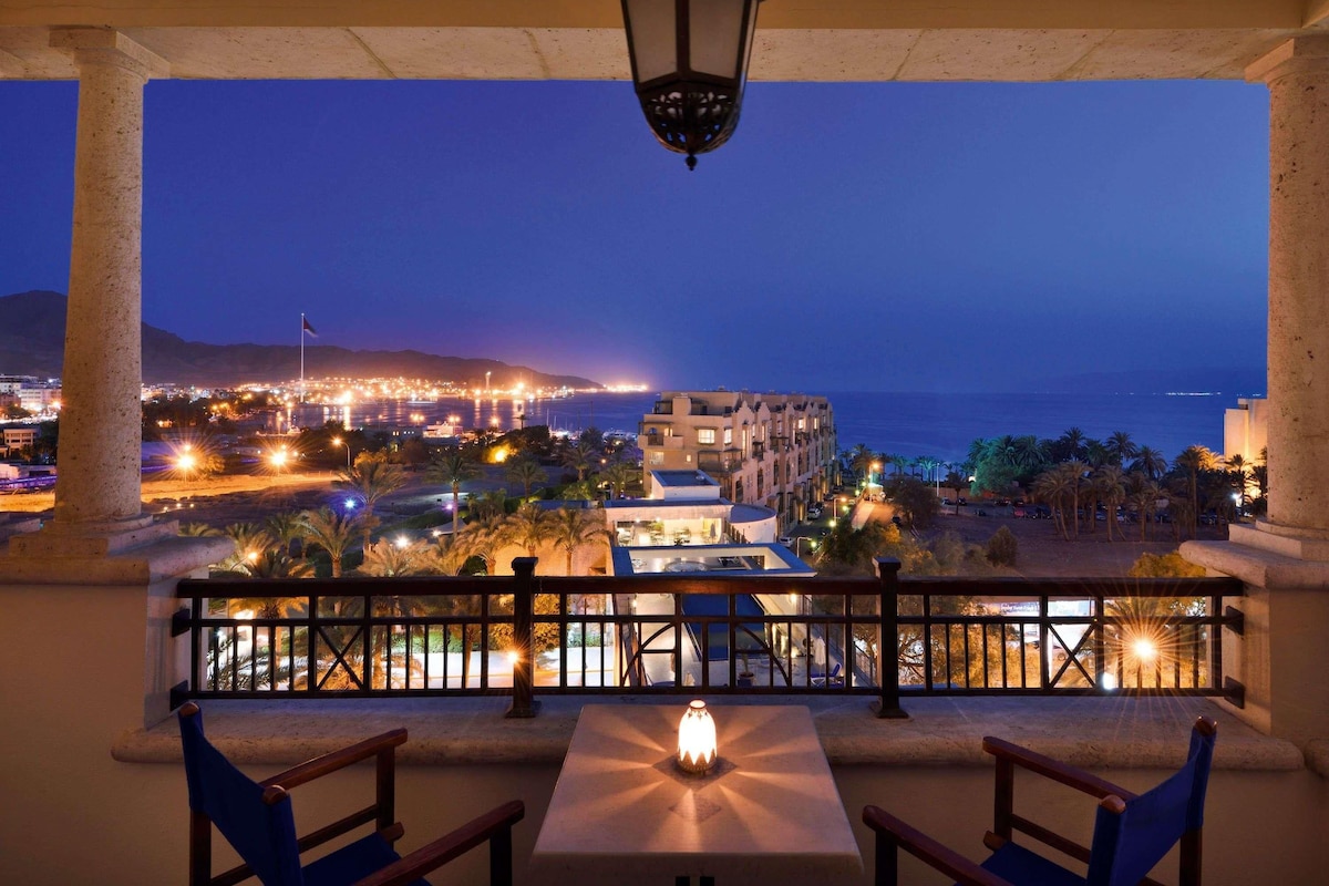 A balcony with a table and chairs, overlooking a cityscape at night.