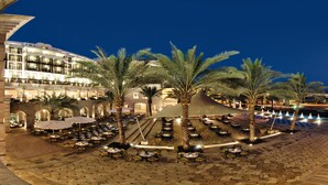 Un patio de hotel con mobiliario exterior, palmeras y una zona de piscina de noche.