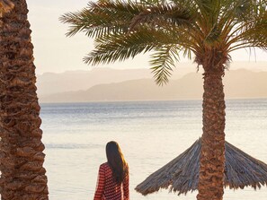 A beach scene with palm trees and a person in a checkered shirt. - Mövenpick Resort & Residences Aqaba (Aqaba)