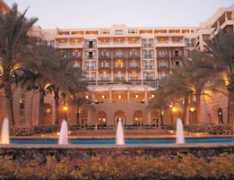 A multi-story hotel with a central courtyard, palm trees, and a pool with fountains.